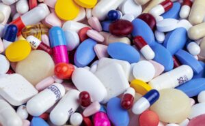Assorted pills, capsules, and tablets in various colors spilling on a surface.