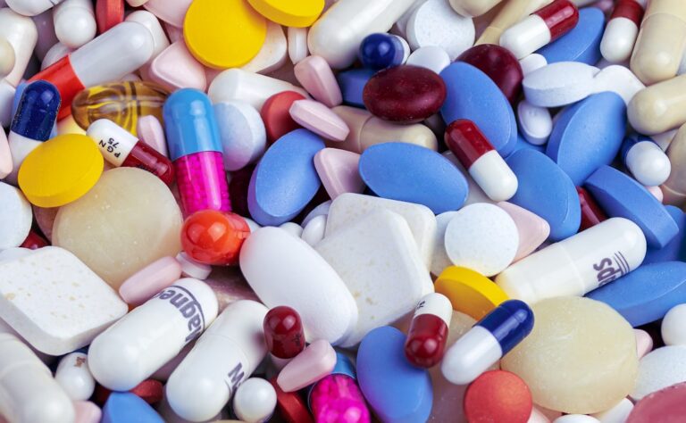 Assorted pills, capsules, and tablets in various colors spilling on a surface.
