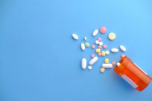 Orange prescription bottle tipped over, spilling assorted colorful pills on a blue surface.