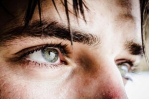 Close-up of a person's green-blue eye, with prominent lashes and eyebrow, looking to the side.