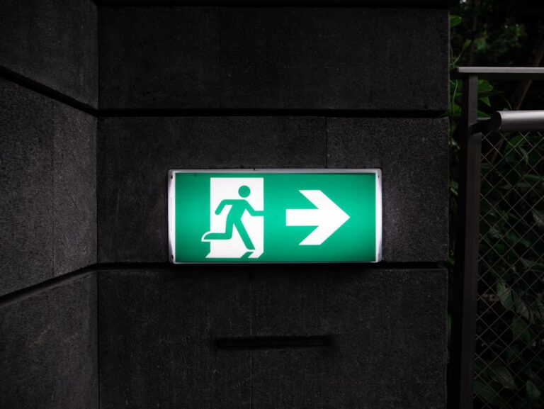 Sickinnyctravelerwhattodo sickday Green emergency exit sign with a running figure and a rightward arrow mounted on a dark wall