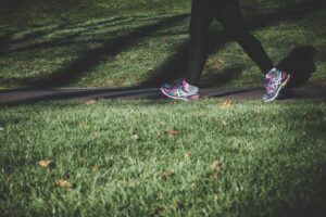 Person wearing colorful running shoes walking on a paved park path with green grass nearby