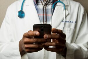 Blog 4 Physician in a white coat with a stethoscope holding and using a smartphone.